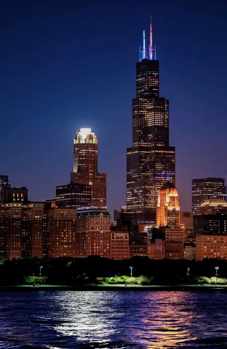 the city skyline is lit up at night with bright lights on it's skyscrapers